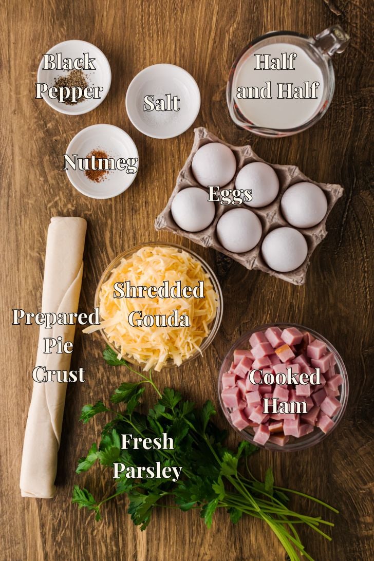 हैम और पनीर के लिए सामग्री काउंटर पर व्यवस्थित की गई है, जिसमें अंडे, आधा-आधा, कटा हुआ हैम, कटा हुआ गौडा और एक डीप-डिश पाई क्रस्ट शामिल है।