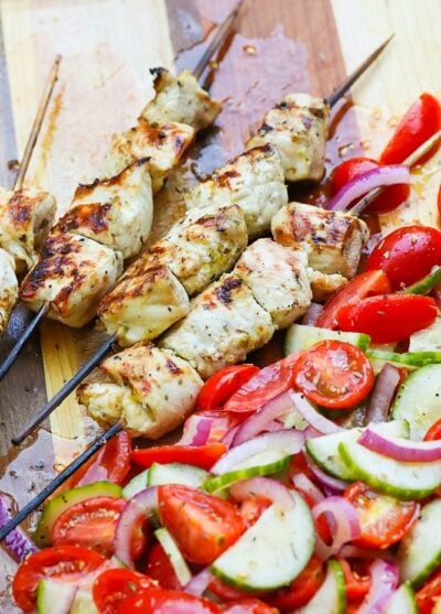 Grilled Chicken Souvlaki Skewers are juicy and tender. Make with lemon juice, oregano, garlic, salt and pepper. Add in a chopped salad with tomatoes, onions and cucumbers and you've got a meal your friends and family will love!