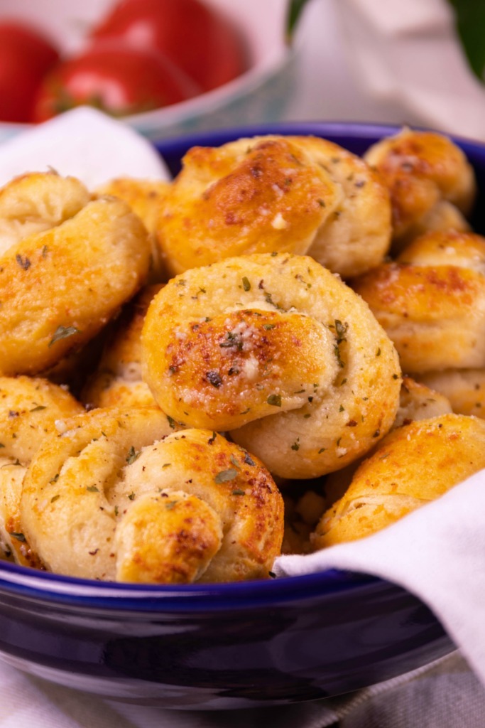 Incredibly easy to make, and ready to serve in less than 20 minutes, these Garlic Knots are seriously delicious! Made with canned biscuits and slathered with butter, garlic, Parmesan cheese, and herbs, they are great as an appetizer served with marinara for dipping, or alongside your favorite recipes at mealtime.