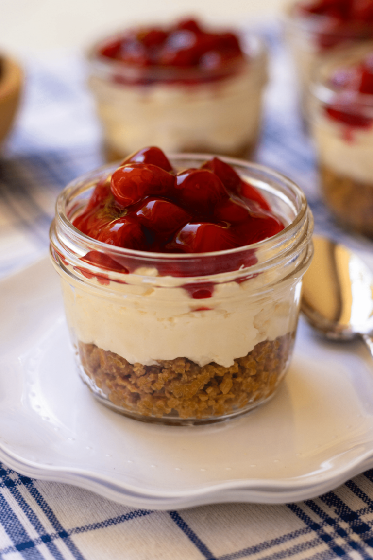 No Bake Cherry Delight In Jars is a yummy, easy to make dessert. A crust made with crushed graham crackers, butter and sugar is layered into small jars then topped with a mixture of cream cheese, powdered sugar and fresh whipped cream all topped with cherry pie filling.