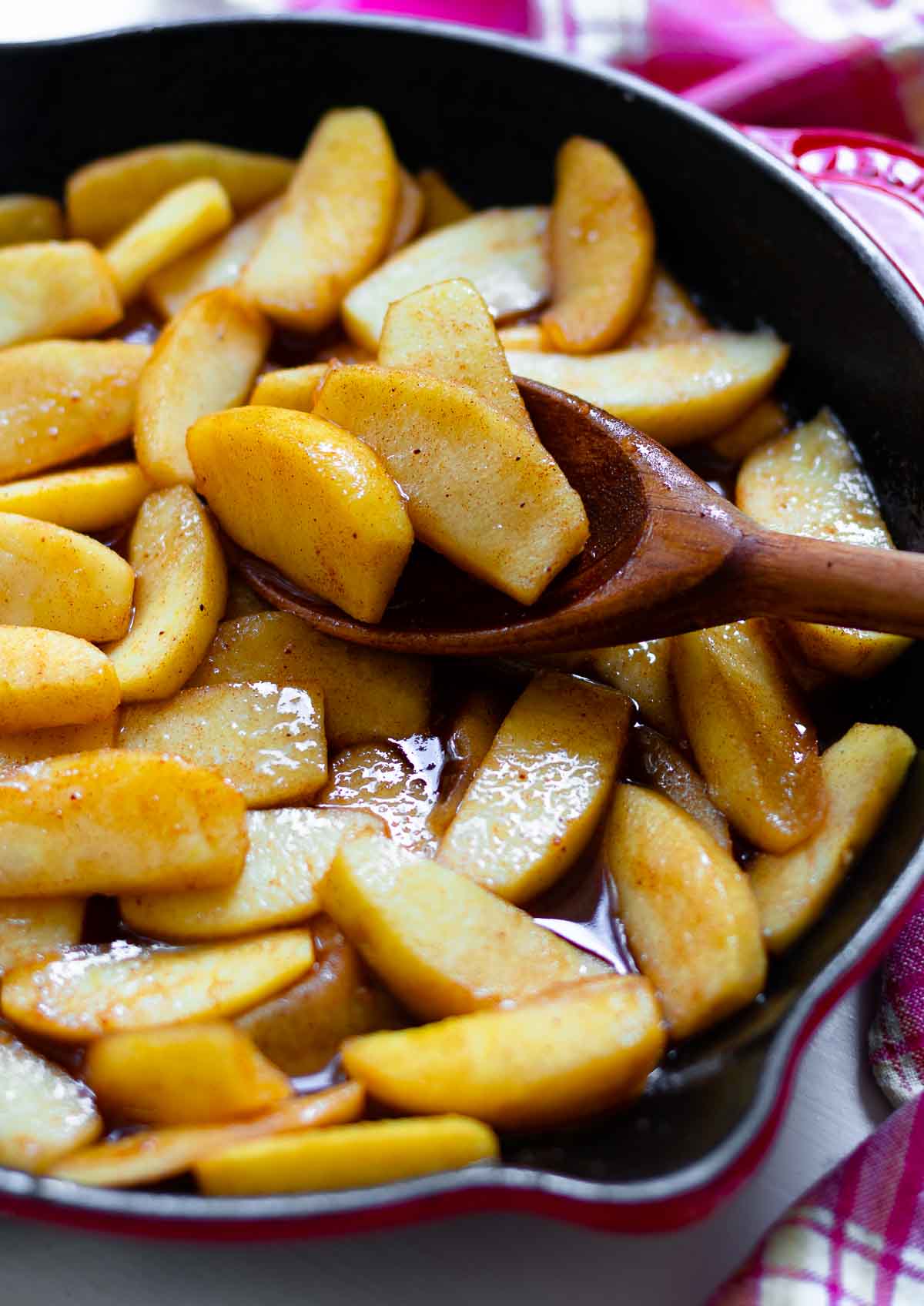 Cinnamon Apples cooked in a cast iron skillet using a wooden spoon.