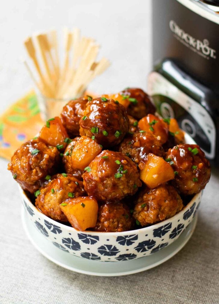 Crock Pot Hawaiian Meatballs in a bowl with the slow cooker and skewers.