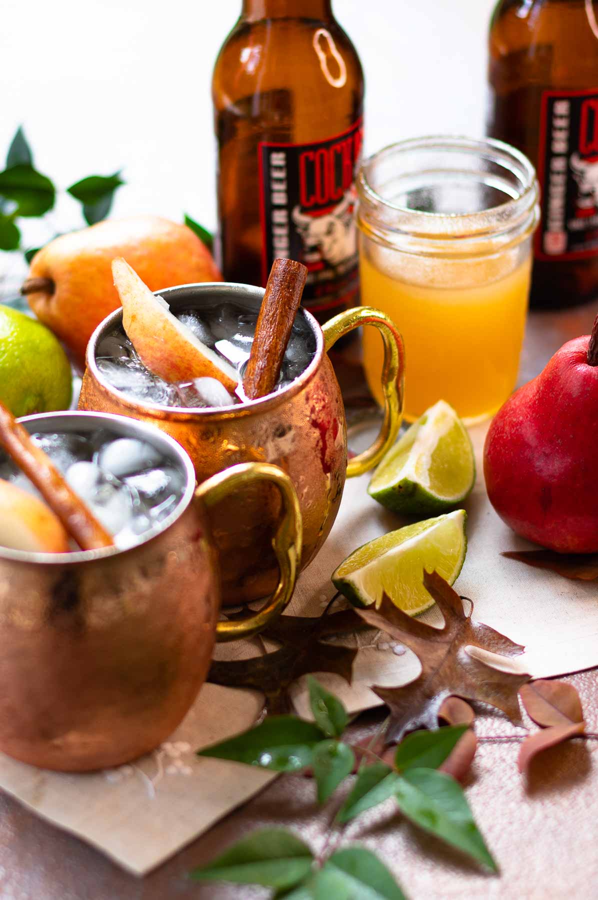 Copper mugs filled with Spiced Pear Moscow Mule drinks with lime and simple syrup.