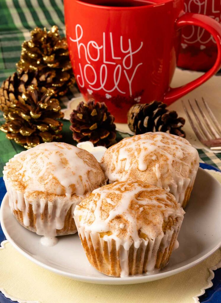 Eggnog Muffins on a white plate with a red mug and pinecones on the table.