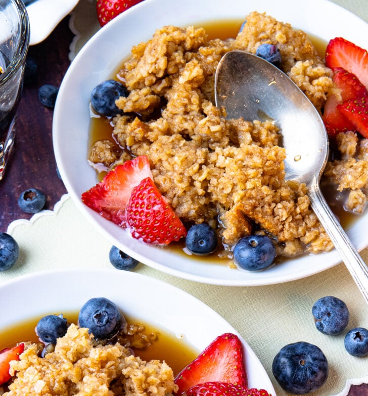 Maple Cinnamon Baked Oatmeal on white plates with fresh blueberries and strawberries.