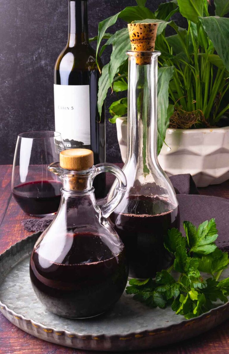 Two glass bottles of homemade red wine vinegar on a metal tray with greenery.