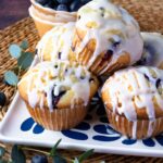 Blueberry Sour Cream Muffins With Lemon Glaze on a plate with fresh blueberries.