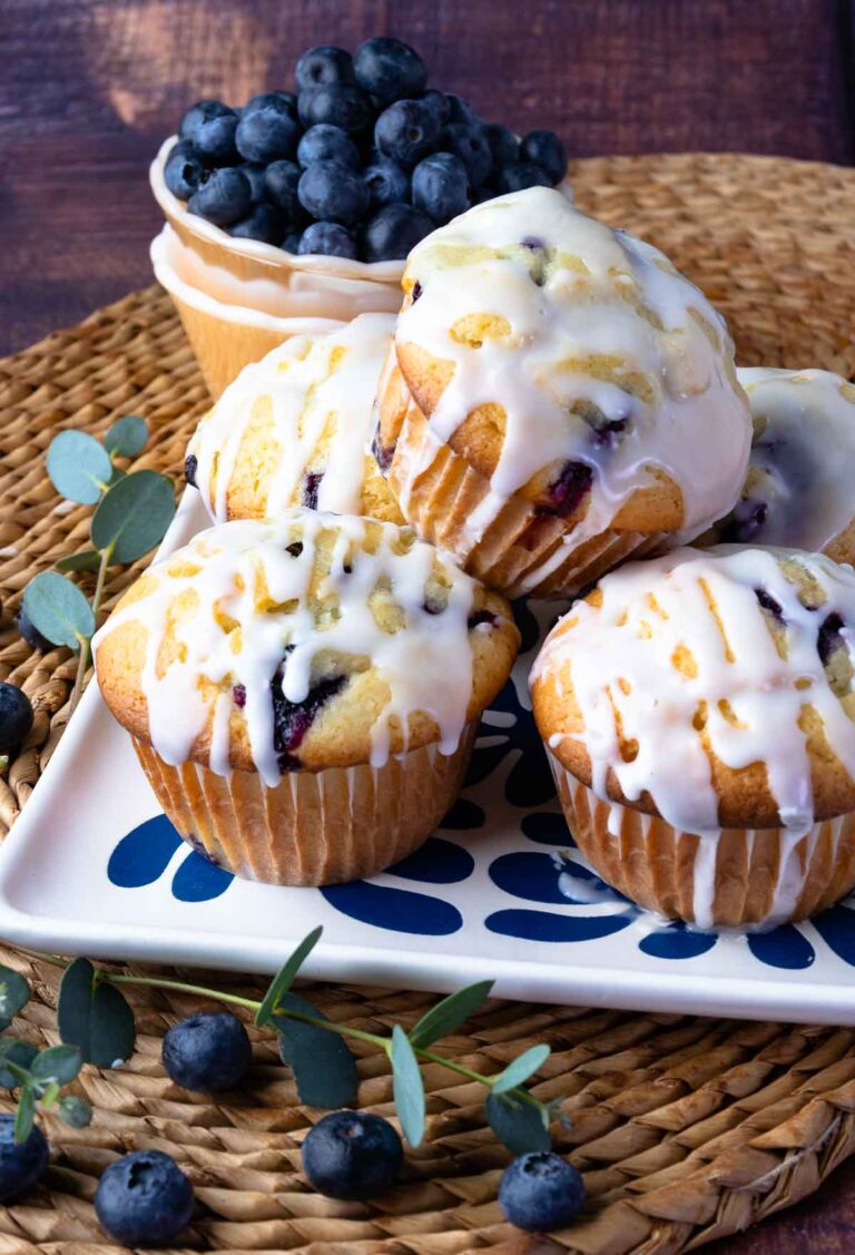 Blueberry Sour Cream Muffins With Lemon Glaze on a plate with fresh blueberries.