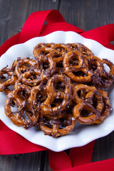 Chocolate Caramel Pretzels with Sea Salt on a white plate with red ribbon decorations.