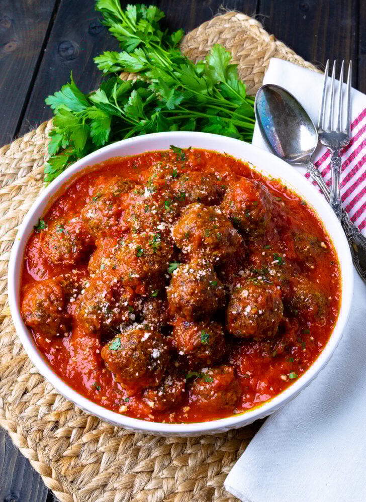 Homemade Meatballs in a white bowle with a napkin, spoon and fork.