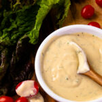 Spoon in a bowl of Garlic Herb Tahini Dressing and Dip with lettuce and tomatoes