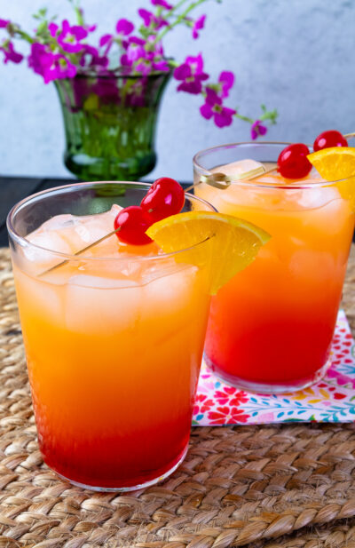 2 pretty glasses of Tequila Sunrise cocktails on placemants with napkins.