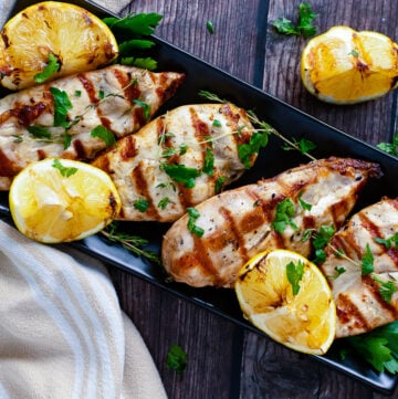 Grilled lemon chicken horz1 served on black platter with charred lemon halves and fresh parsley garnish on wooden table