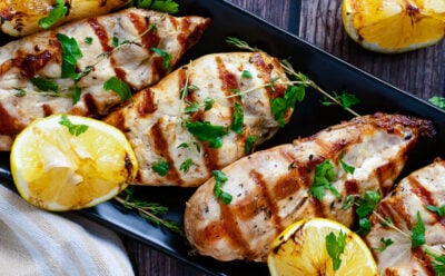 Grilled lemon chicken horz1 served on black platter with charred lemon halves and fresh parsley garnish on wooden table