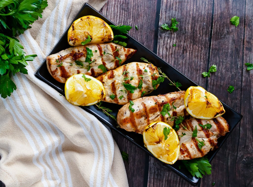 Grilled lemon chicken horz2 on black plate with charred lemon slices and fresh parsley garnish on wooden table