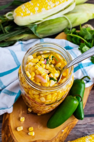 Pickled Corn with red onions and jalapenos in a jar served with a spoon.
