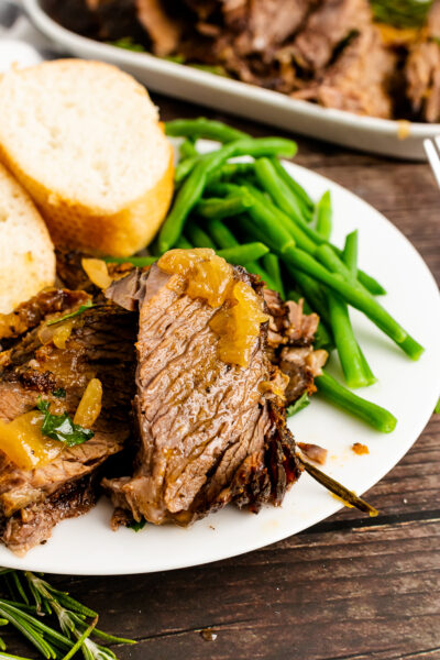 Sliced Pot Roast with onion, green bean and bread on a white plate.