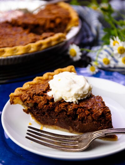 Slice of Chocolate Chess Pie with pecans on a white plate with a fork.