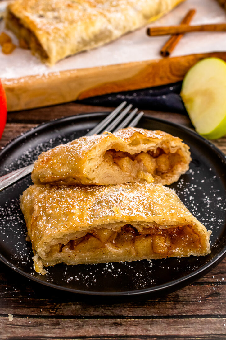 2 slices of Apple Strudle on a black plate with fork.