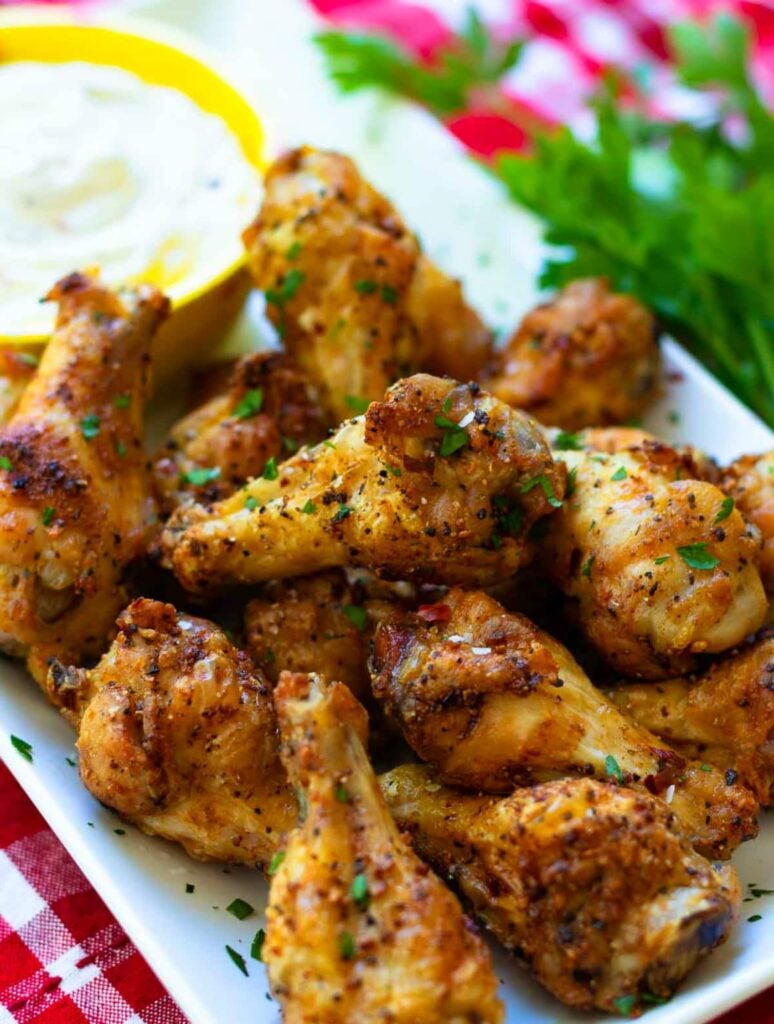 Golden AF chicken wings close boosted 2, seasoned with black pepper and fresh parsley, served on white plate with lemon and dipping sauce