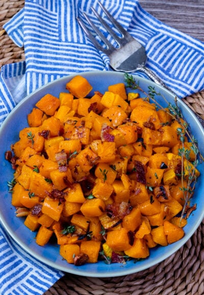Blue bowl with roasted butternut squash with fresh thyme and a fork for serving.