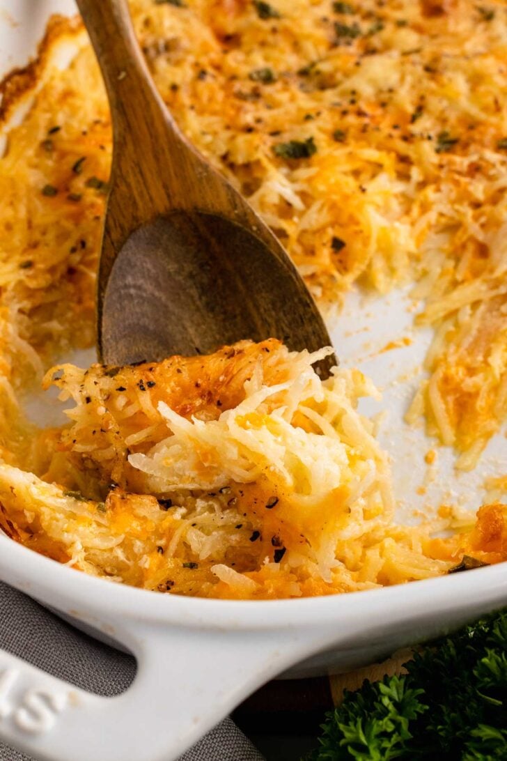 Wooden spoon with cheesy hash brown casserole.