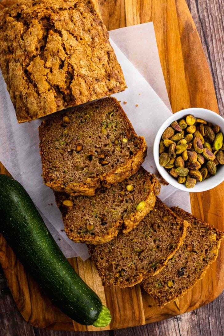 Slices of Zucchini Bread on a cutting board with shelled pistachios.