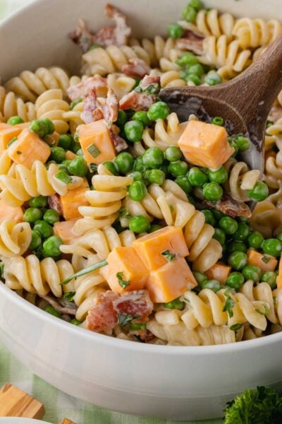 Bacon ranch pasta salad being tossed with a wooden spoon.