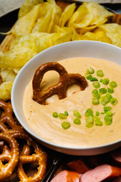 Large white bowl with Beer Cheese Dip topped with green onions served with sausage and pretzels.