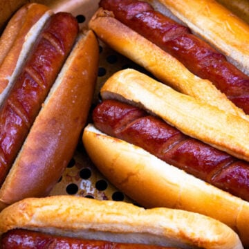 Cropped air fryer hot dogs 8, cooked sausages nestled in toasted buns inside mesh basket, overhead view