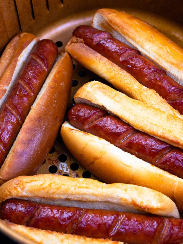 Cropped air fryer hot dogs 8, cooked sausages nestled in toasted buns inside mesh basket, overhead view
