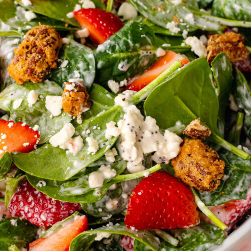 Strawberry Spinach Salad in a white bowl with fresh spinach, sliced strawberries, crumbled feta cheese, and crispy candied nuts