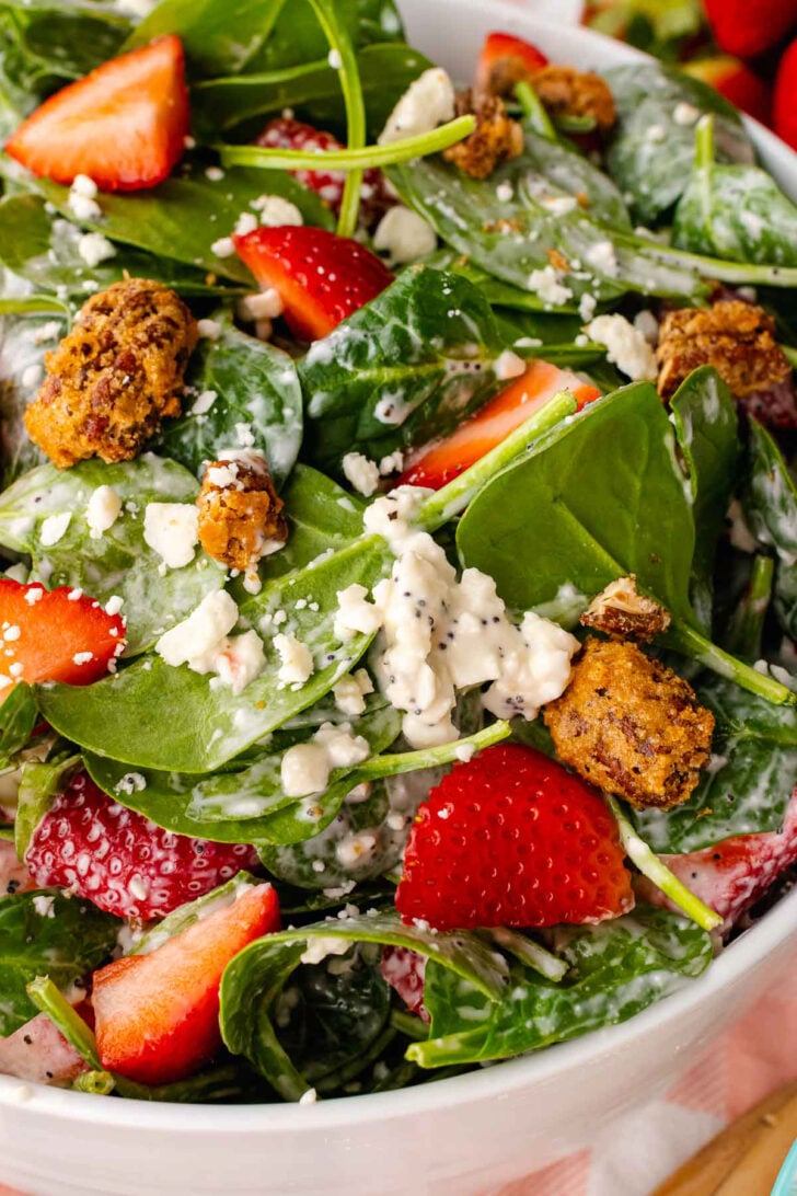 Strawberry Spinach Salad in a white bowl with fresh spinach, sliced strawberries, crumbled feta cheese, and crispy candied nuts