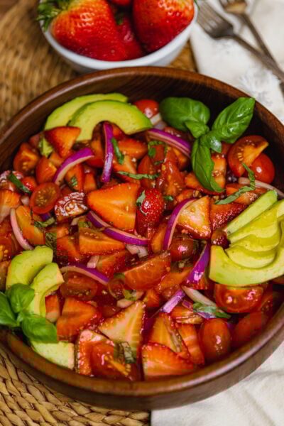 Wooden bowl with strawberry tomato avocado salad served with a silver spoon as a delicious side dish.