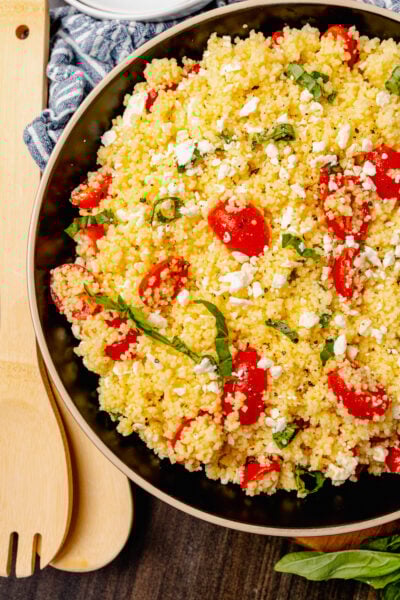 Big bowl of couscous salad with feta, tomatoes and fresh basil served as a side dish for lunch, dinner or at a picnic, cookout or family gathering.