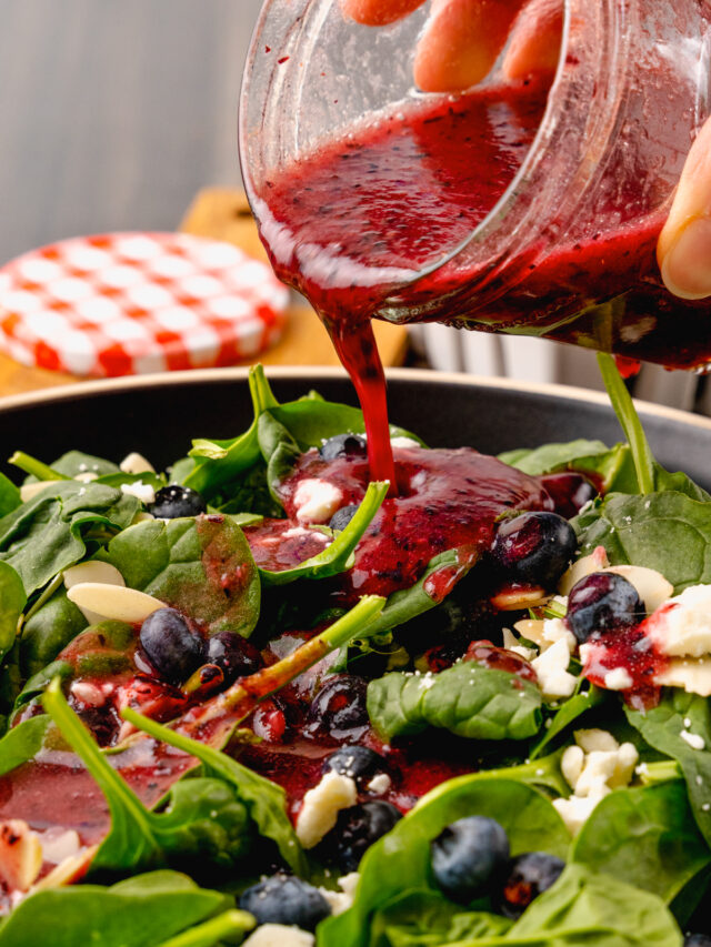 Jar of homemade blueberry vinaigrette salad dressing poured over fresh spinach, sliced almonds and feta cheese for a delicious, refreshing salad.