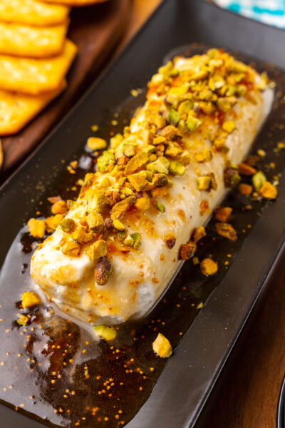 Goat cheese log with fig jxaam, honey and sprinked with chopped pistachios served on a black platter for cocktails.