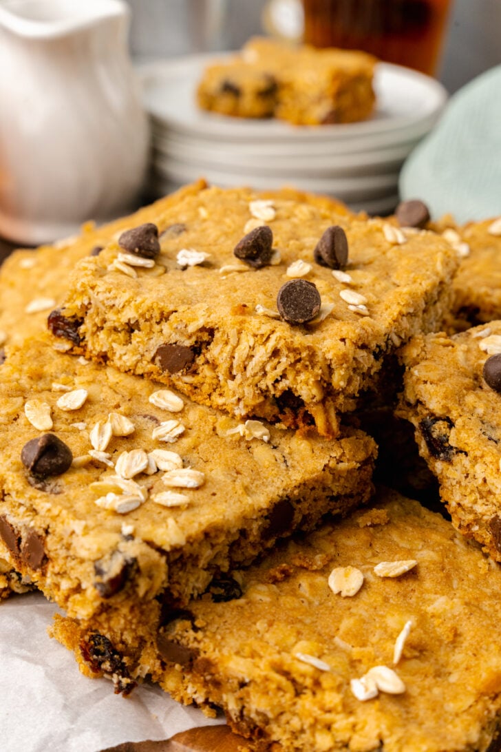 Oatmeal chocolate chip cookie bars, baked and cut into squares stacked on a white plate served along side cup of tea.