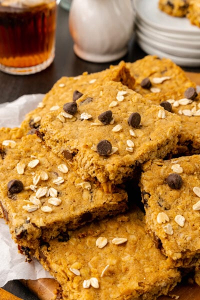 Oatmeal chocolate chip cookie bars stacked on a white plate served along side cup of tea.