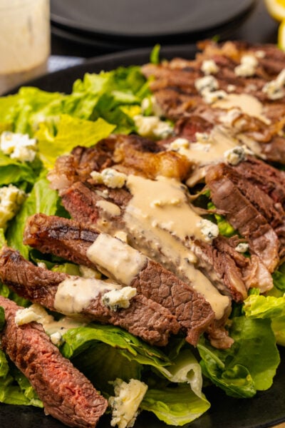 Grilled Steak Salad with blue cheese, creamy vinaigrette salad dressing and chopped romaine lettuce with blue cheese crumbles served on a black platter.