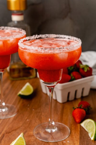 Sugar, salt rimmed glass rimmed glass with a fresh strawberry margarita with ice made with fresh fruit and limes.