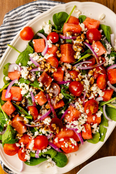 White serving platter loaded with fresh watermelon, grape tomatoes, red onion, spinach and feta cheese is an easy to make side dish for any spring or summer gathering.