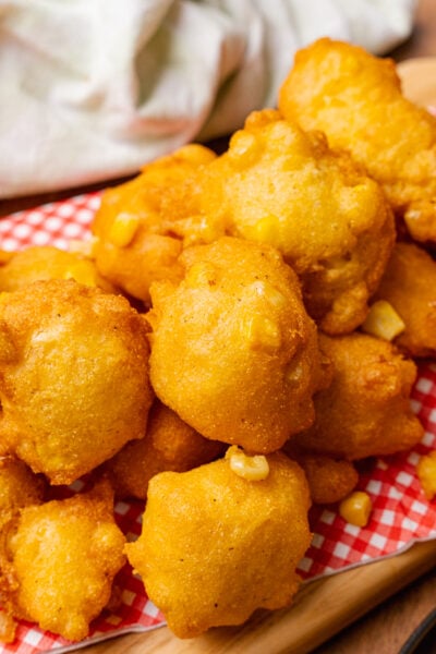 Stack of fried corn fritter stacked on a red and white paper napkin on a wooden serving board.