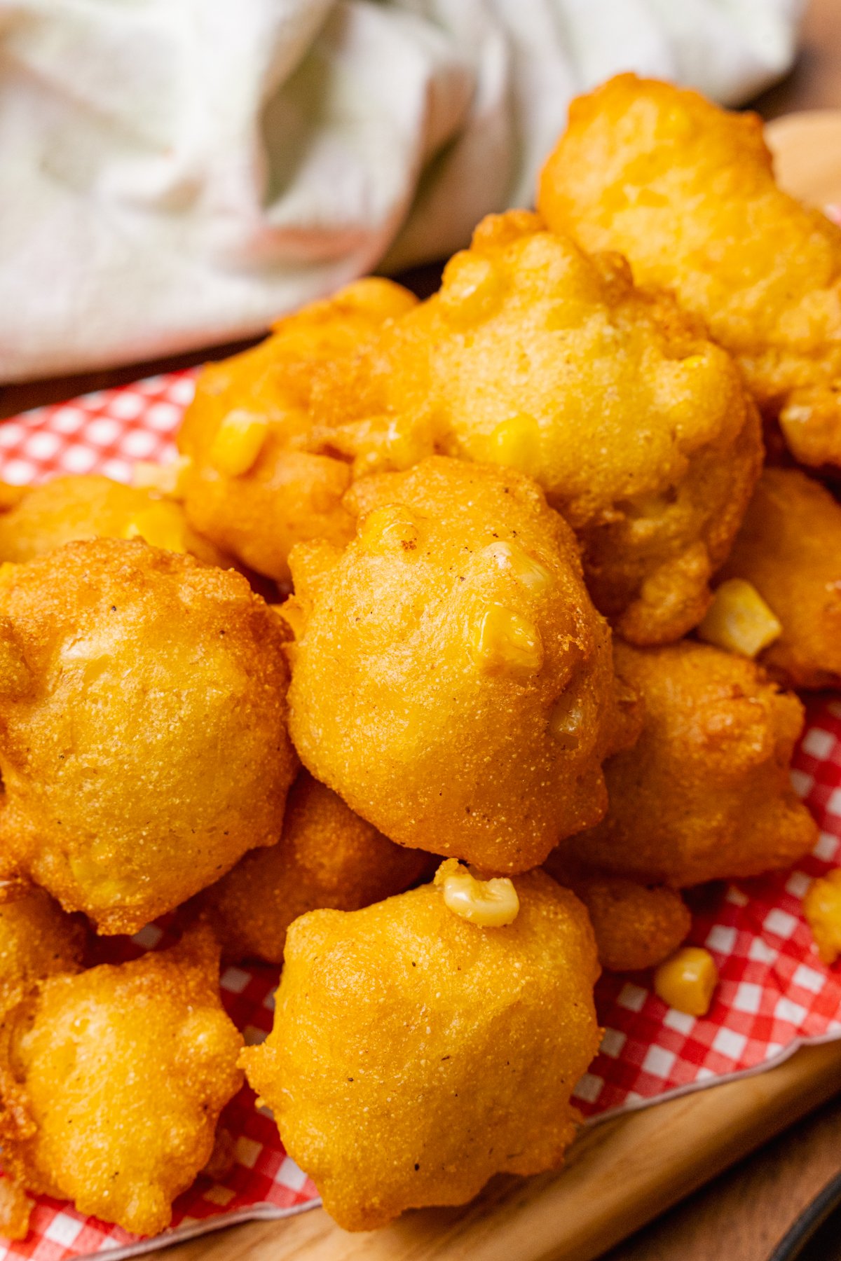 Stack of fried corn fritter stacked on a red and white paper napkin on a wooden serving board.