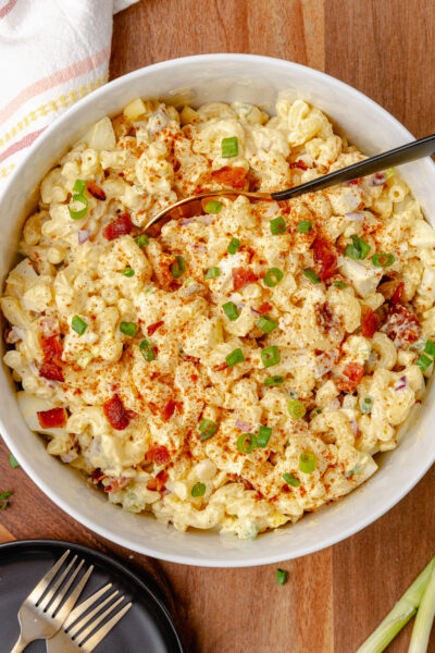 Creamy and full of flavor, Deviled Egg Pasta Salad is a side dish classic that perfect for any family gathering, cookout, or potluck. Made with elbow macaroni, boiled eggs, celery, bacon and topped with green onions all in a delicious mayonnaise based dressing topped with a sprinkle of paprika served in a white bowl.