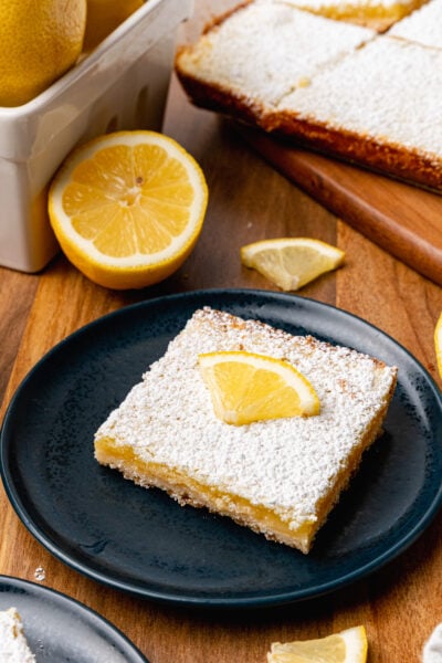 A lemon bar topped with a lemon slice served on a black plate for dessert.