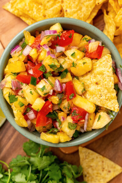 Small bowl of fresh pineapple salsa served with lime wedges and corn tortilla chips.