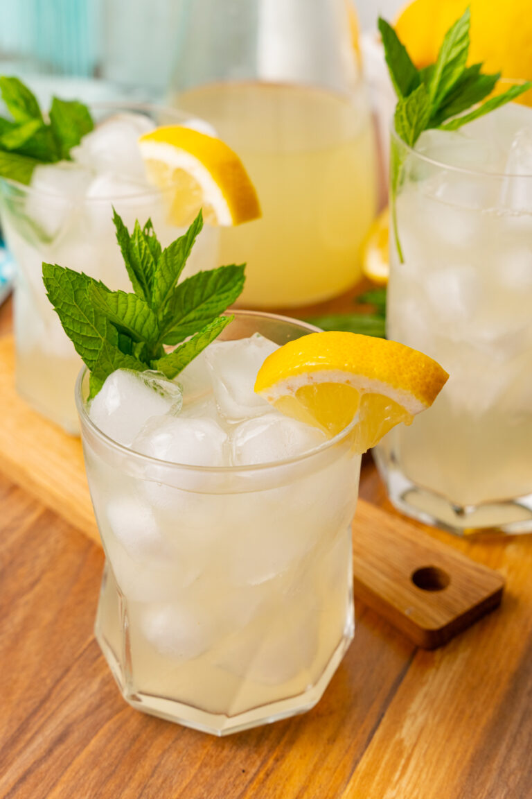 Glass of homemade lemonade with a lemon wedge and sprig of mint on a wooden board.