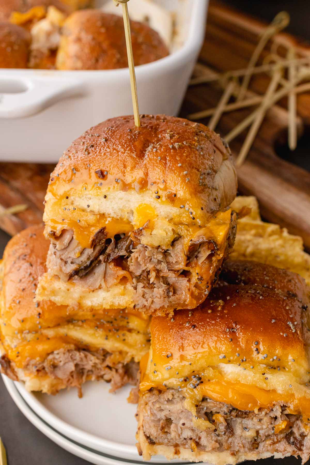 Roast Beef and Cheese Sliders stacked on a white plate on a wooden cutting board.
