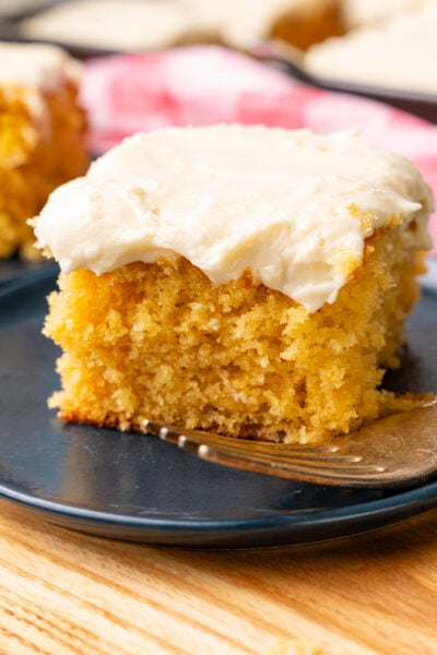 Slice of caramel snack cake with light, creamy caramel icing on a blue plate served with a silver fork.